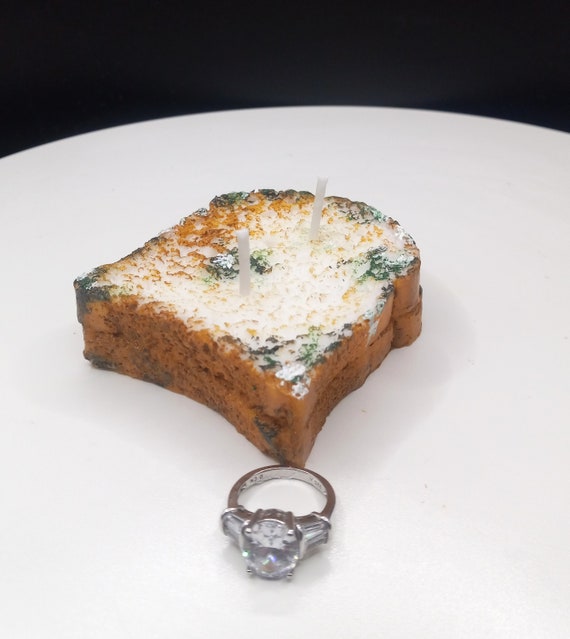 A hand-poured candle sculpted to look like a genuinely disgusting piece of moldy toast — it's gross, it's funny, and it's weirdly impressive craft.