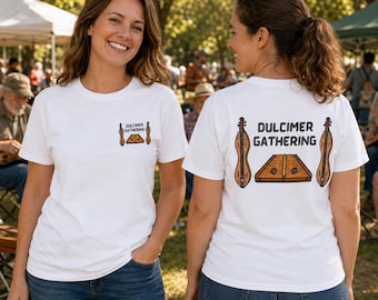 May include: A white t-shirt featuring a small graphic on the front left chest and a larger version on the back. The design includes two brown stringed dulcimer instruments flanking a trapezoidal dulcimer with the text Dulcimer Gathering.