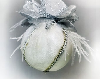 Puede incluir: Adorno navideño blanco con un lazo de brillo plateado y plumas blancas.
