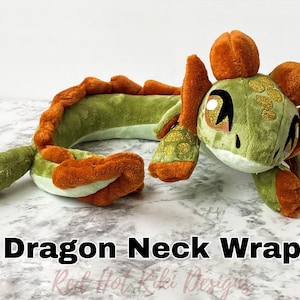 Könnte beinhalten: Ein grüner und orangefarbener Plüsch-Drachen-Nackenwärmer. Der Drache hat große Augen, ein detailliertes Gesicht und einen langen, geschwungenen Körper. Der Text "Dragon Neck Wrap" ist in schwarzer Schrift dargestellt.