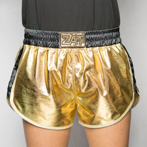 May include: Gold and black boxing shorts with a white trim and the word "ZAT" on the waistband.