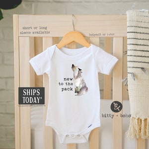May include: White baby onesie with a watercolor illustration of a wolf howling. The onesie has the text "new to the pack" printed on it.