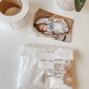 May include: A white paper bag with a brown and white patterned fabric inside. The bag has a white label with the text "bitty + boho" printed on it.