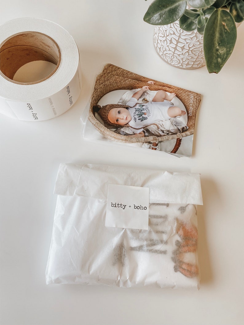 May include: A white paper bag with a brown and white patterned fabric inside. The bag has a white label with the text "bitty + boho" printed on it.