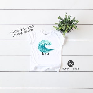 May include: White t-shirt with a blue watercolor wave graphic and the word "bro" printed below. The shirt is available in short or long sleeves.