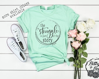 May include: A light green t-shirt with a black circle graphic that says "the struggle is part of the story #TINE".