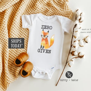 May include: White baby onesie with a watercolor illustration of a fox wearing glasses and the text "ZERO GIVEN".
