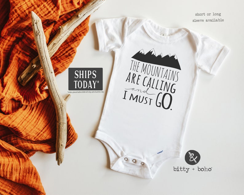 May include: White baby onesie with black text that reads "The Mountains Are Calling and I Must Go."  The text is surrounded by a graphic of black mountains. The onesie has a snap closure and is available in short or long sleeves.