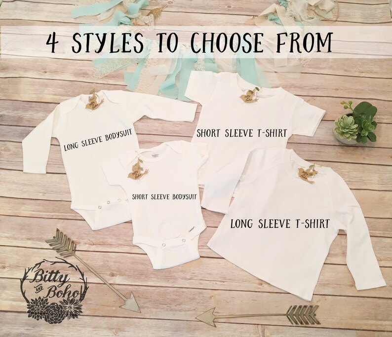 K&ouml;nnte beinhalten: Vier wei&szlig;e Babykleidungsst&uuml;cke: ein lang&auml;rmliger Body, ein kurz&auml;rmliger Body, ein kurz&auml;rmliges T-Shirt und ein lang&auml;rmliges T-Shirt. Der Text "4 STYLES TO CHOOSE FROM" steht oben. Das Bitty and Boho-Logo befindet sich unten.