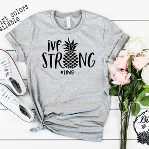 May include: Gray t-shirt with black text that reads "ivf strong #1in8" and a pineapple graphic with hearts.