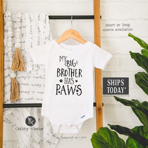 May include: White baby onesie with black text that reads "My Big Brother Has Paws".