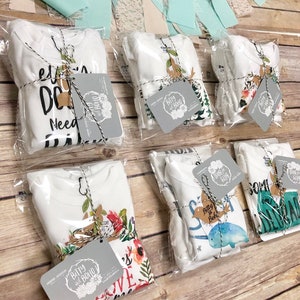 Puede incluir: Bodies blancos para beb&eacute;s empaquetados en pl&aacute;stico transparente, atados con hilo y etiquetas. Los bodies tienen varios dise&ntilde;os, incluyendo patrones florales, gr&aacute;ficos de animales y texto. Las etiquetas dicen "Bitty and Boho".
