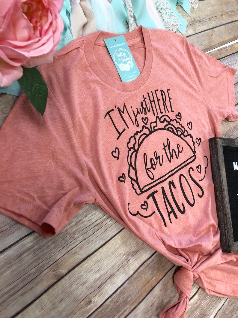 May include: A pink t-shirt with the text "I'm just here for the tacos" in black lettering with a taco graphic and hearts.