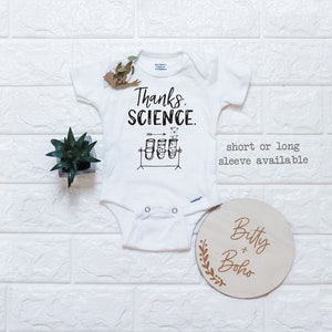May include: White baby onesie featuring the text "Thanks, Science." and a graphic of three test tubes with hearts floating above them. The onesie is available in short or long sleeves.