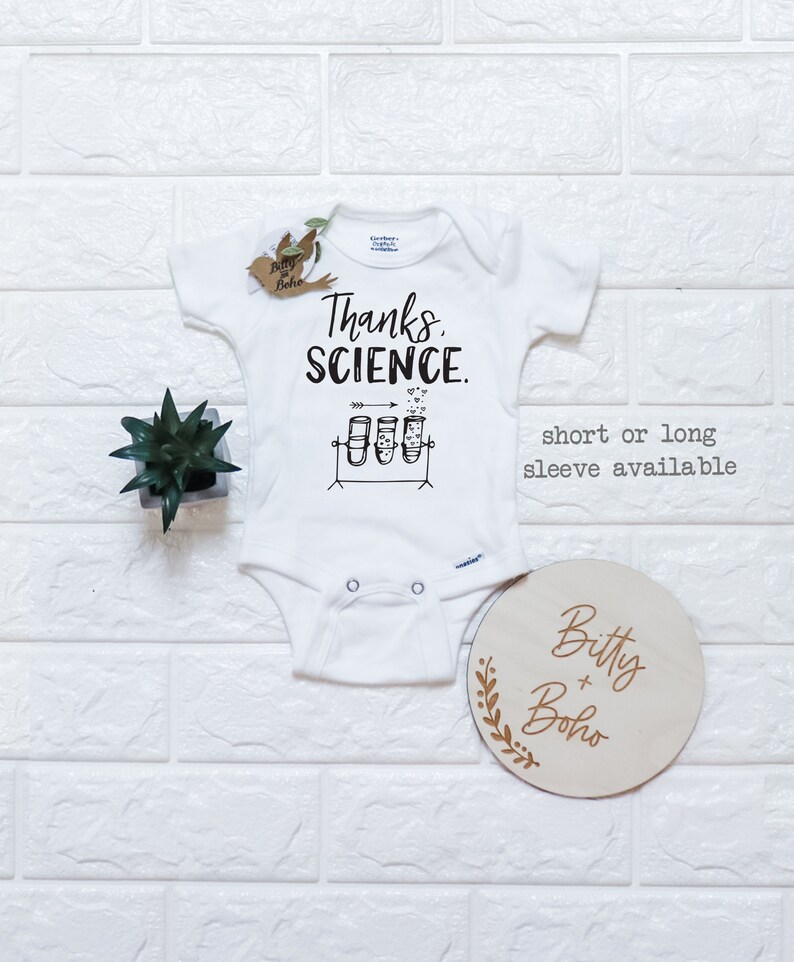 May include: White baby onesie featuring the text "Thanks, Science." and a graphic of three test tubes with hearts floating above them. The onesie is available in short or long sleeves.