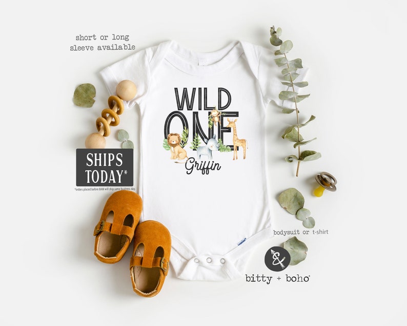 K&ouml;nnte beinhalten: Wei&szlig;er Baby-Strampler mit schwarzem Text, der "WILD ONE" lautet, und dem Namen "Griffin" in schwarzer Schrift. Der Strampler zeigt eine Grafik von Dschungeltieren, darunter ein L&ouml;we, eine Giraffe, ein Elefant und ein Affe.