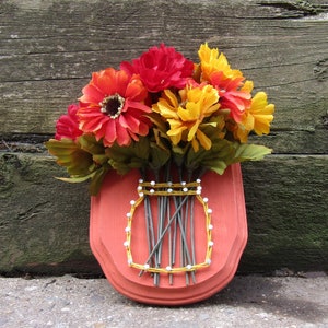 May include: A red wooden vase with a yellow string design, holding a bouquet of orange, yellow, and red silk flowers.