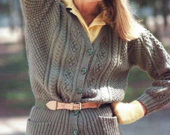 May include: A woman wearing a gray knitted cardigan with a cable knit pattern, a yellow knitted hat, and a brown leather belt. The cardigan has a v-neck and buttons down the front.