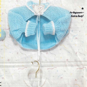 Könnte beinhalten: Zwei gestrickte Baby-Pullover, einer hellblau und einer weiß, mit einem weißen Band, das um den Hals jedes Pullovers gebunden ist. Die Pullover liegen auf einem weißen Hintergrund mit einem bunten Konfetti-Muster. Der Text "tiny sizes for early arrivals" ist auf einem gelben Etikett mit einem Comic-Bären gedruckt.