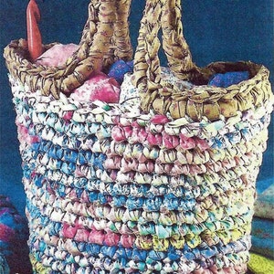 Pode incluir: Uma cesta de crochê feita com retalhos de tecido em tons de rosa, azul e branco. A cesta tem uma alça trançada e está cheia de retalhos de tecido coloridos.