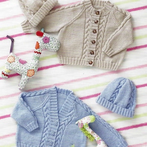 Puede incluir: Dos cárdigans de punto para bebé con cierre de botones, uno en beige y otro en azul claro, con gorros de punto a juego. Los cárdigans presentan un patrón de punto de cable.