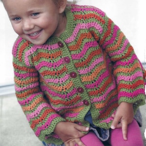 Op de afbeelding: Een kind draagt een gebreide cardigan met groene, roze, oranje en rode strepen met knopen.
