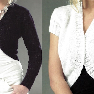 May include: Two cropped cardigans, one black and one white, with a V-neck and long sleeves. The black cardigan is worn over a white tank top and white pants. The white cardigan is worn over a black tank top and black pants.