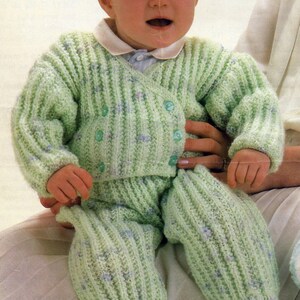 May include: A baby wearing a light green knitted cardigan and matching pants with a white collar and buttons. The outfit has a textured knit pattern and blue accents.