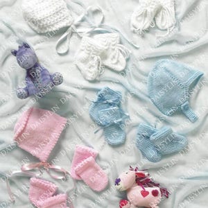 Puede incluir: Un conjunto de gorros y patucos de punto para bebé en rosa, azul y blanco. Los gorros tienen una parte superior puntiaguda y los patucos tienen un diseño sencillo. También hay dos juguetes de peluche, uno morado y otro rosa.