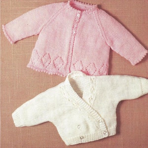May include: Two knitted baby cardigans, one pink with a lacy trim and one white with a cable knit design.