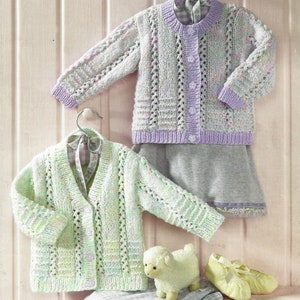 May include: Two knitted baby cardigans with a lacy pattern. One cardigan is light green with white and pink flecks, the other is light purple with white and pink flecks.