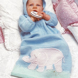 Könnte beinhalten: Ein hellblauer gestrickter Babyschlafsack mit einem rosafarbenen Elefantenmuster. Der Schlafsack hat eine Kapuze und wird von einem Baby getragen, das einen Beißring hält.