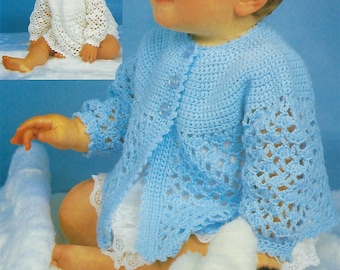 May include: A baby wearing a light blue crocheted cardigan with a white crocheted lace trim. The cardigan has a button closure and is open in the front. The baby is sitting on a white fluffy surface and holding a white and black stuffed animal.
