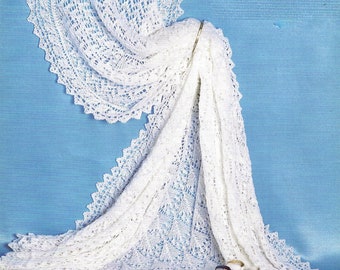 May include: A white crocheted baby blanket with a delicate lace pattern. The blanket is draped over a blue surface and has a pair of white baby shoes with black ribbon ties.