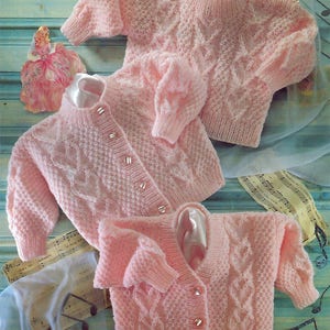 May include: Three pink knitted baby cardigans with a cable knit pattern and pearl buttons.