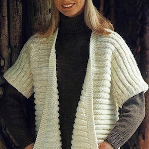Peut inclure: Un cardigan blanc en tricot avec un col en V et des manches courtes. Le cardigan a une texture côtelée et comporte deux poches sur le devant.