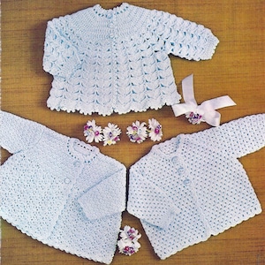 May include: Two crocheted baby sweaters in light blue. One sweater has a lacy pattern and the other has a textured stitch.