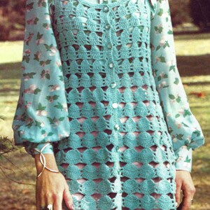 May include: A vintage turquoise crochet dress with a floral print blouse underneath. The dress features a button-up front and a scalloped hem. The blouse has long sleeves and a collared neckline. The overall style is reminiscent of the 1970s.