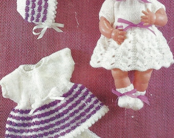 May include: A knitted doll outfit set in white and purple. The set includes a dress with a striped skirt, a hat, booties, and socks.