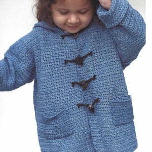 Può includere: Una giacca con cappuccio in crochet blu con chiusure a bottone nere e due tasche. La giacca è indossata da un bambino piccolo.