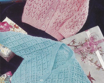 May include: Two knitted baby cardigans, one in pink and one in light blue, with a button-up front and a delicate lace pattern.