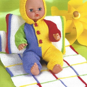 May include: A knitted doll wearing a multi-colored knitted outfit with a yellow knitted hood. The doll is sitting on a white and colored knitted blanket.