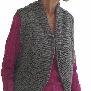 Könnte beinhalten: Eine graue Strickweste mit Schalkragen. Die Weste wird über einem rosa Langarmshirt und einer dunkelblauen Jeans getragen.