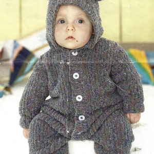 May include: A baby wearing a gray knitted hooded jumpsuit with bear ears. The jumpsuit has a button closure and a textured knit pattern.