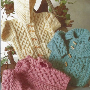 May include: Three knitted baby sweaters in different colors: cream, pink, and teal. Each sweater features a cable knit pattern and wooden buttons.