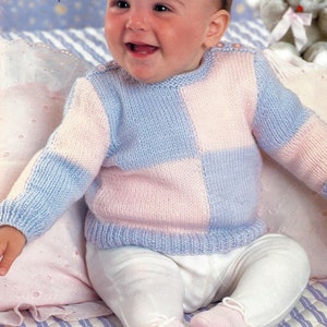 May include: A baby wearing a blue and pink checkered knitted sweater. The sweater has a round neckline and long sleeves.