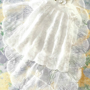 May include: White crocheted baby blanket with a delicate lace pattern. The blanket is folded in half and has a small, ornate silver box on top.