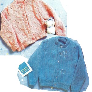 Peut inclure: Deux cardigans en tricot pour bébé, l'un rose avec un motif de câble et l'autre bleu avec une texture lisse. Les deux cardigans ont des fermetures à boutons.