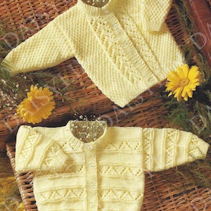 Puede incluir: Dos cárdigans de punto amarillo para bebé con cierre de botones y un delicado patrón de encaje. Los cárdigans están colocados sobre una cesta tejida.