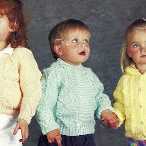 Puede incluir: Tres niños con suéteres de punto en diferentes colores: amarillo, verde claro y azul claro. Los suéteres tienen un patrón de punto de cable.